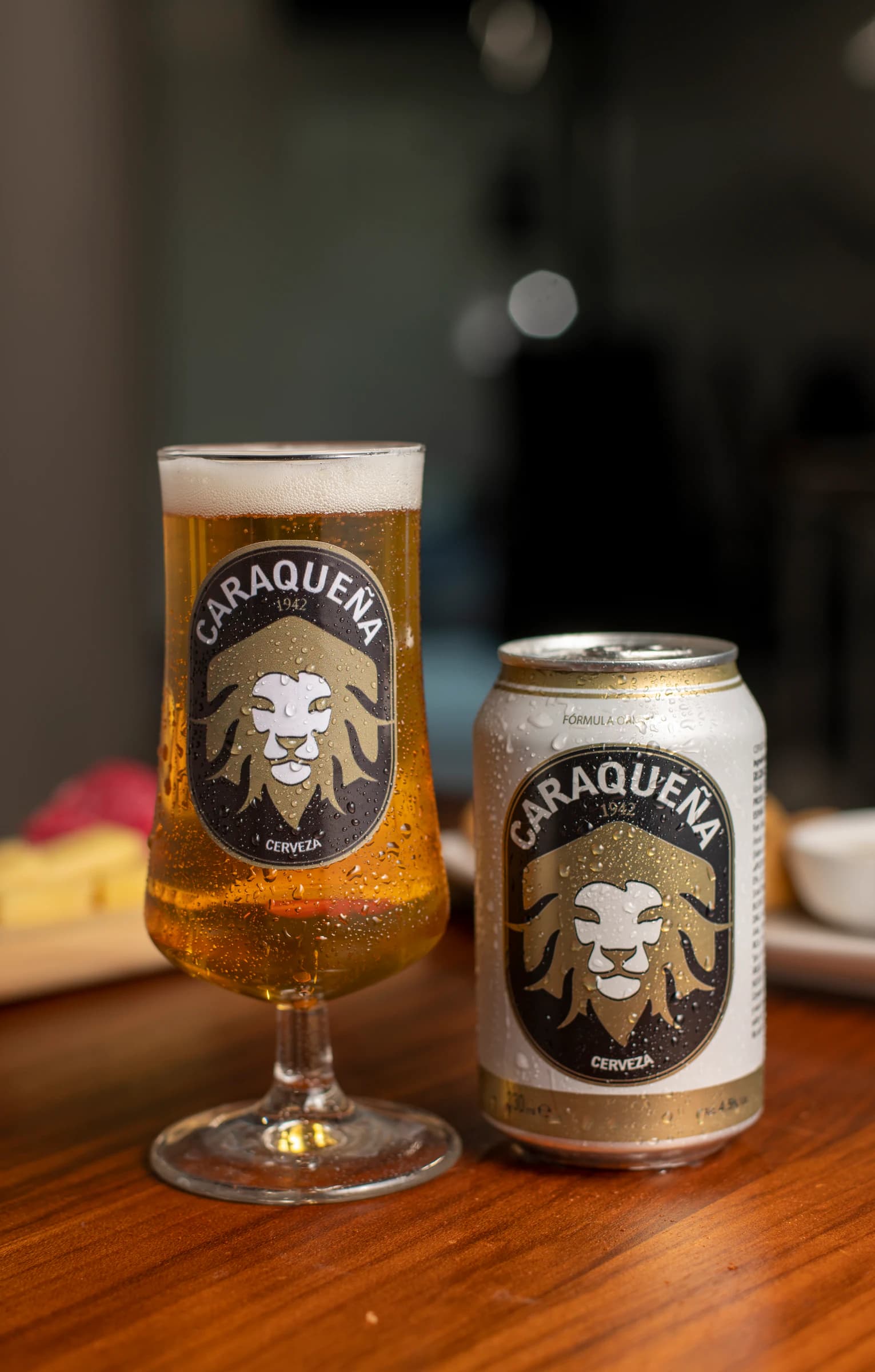 Copa y lata de Cerveza Caraqueña sobre una mesa de madera